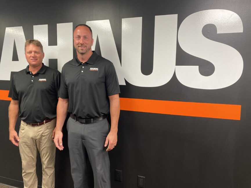 Brian Keiser (right) and Chuck Haager (left) standing in front of a wall with a large Ahaus logo.